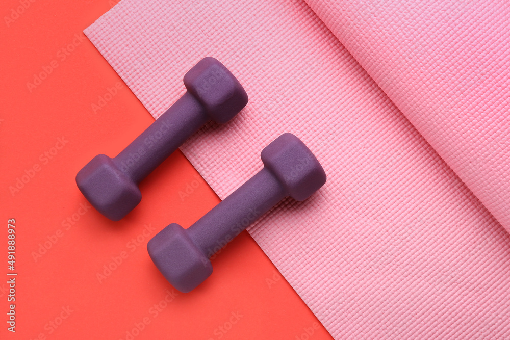 Stylish dumbbells and fitness mat on red background