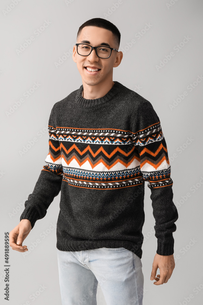 Handsome young Asian man in knitted sweater on grey background