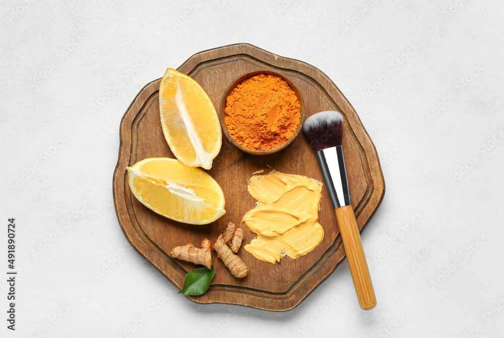 Wooden board with ingredients for turmeric mask and makeup brush on light background