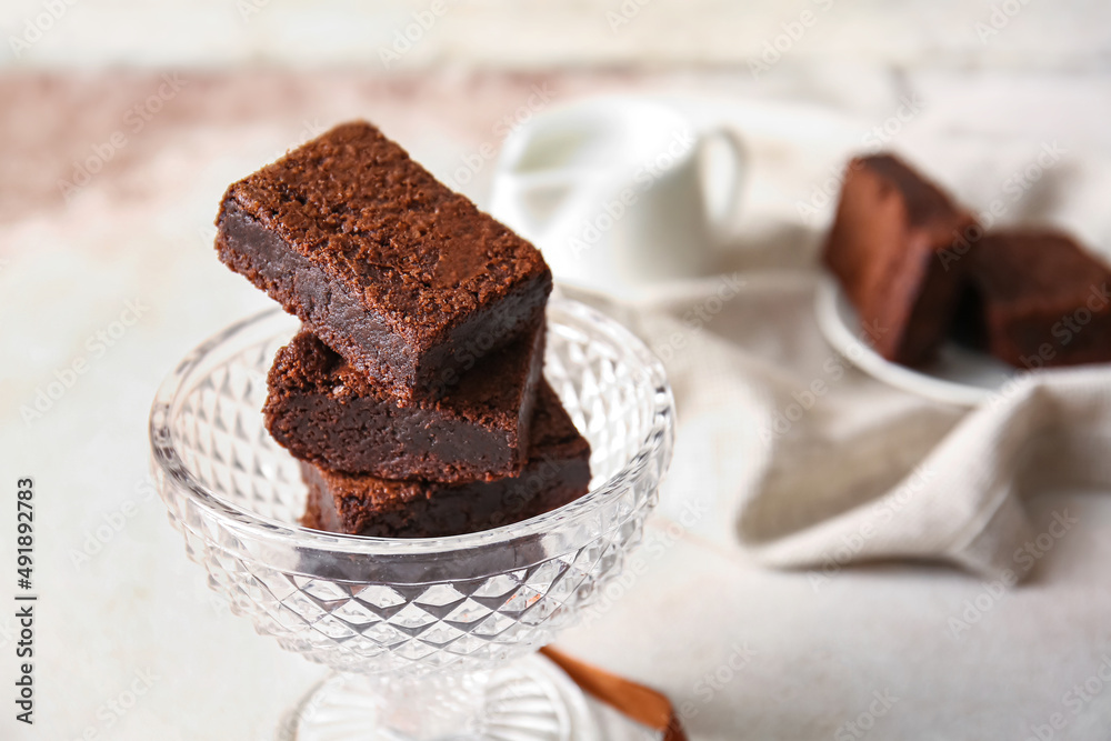 Glass bowl with pieces of delicious chocolate brownie on light background