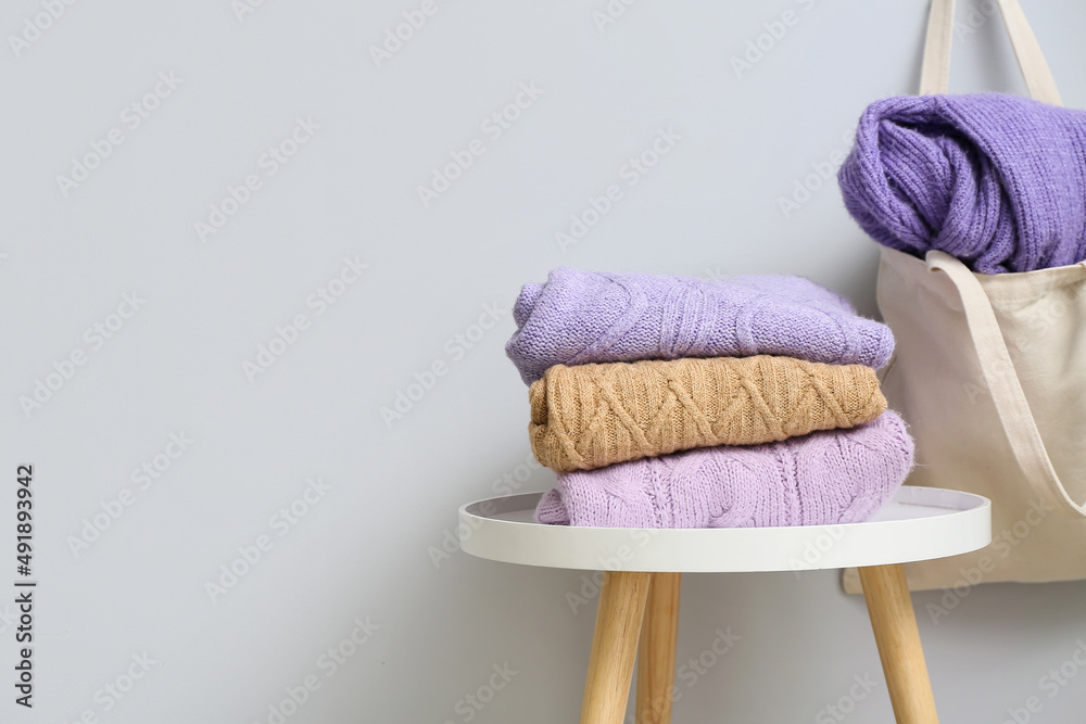 Table with knitted sweaters and bag hanging on light wall