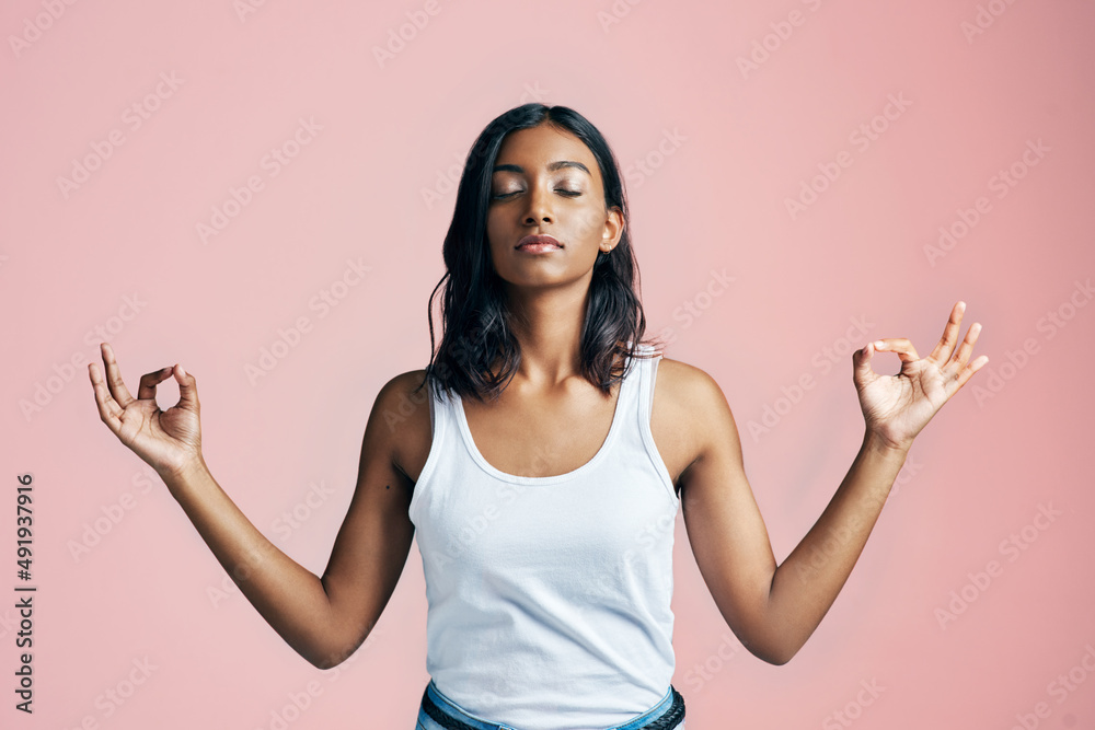 Namaste. Studio shot of a beautiful young woman meditating against a pink background.