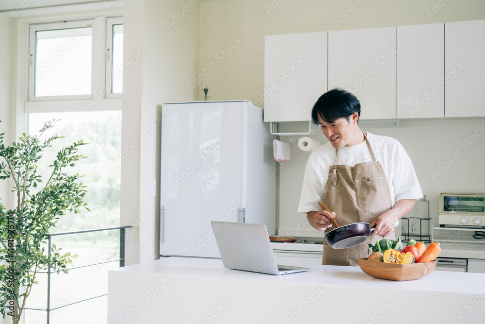 パソコンを見ながら料理する男性（笑顔）
