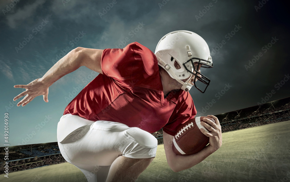 American football sportsman player with ball in action on stadium under lights of background. Sport,