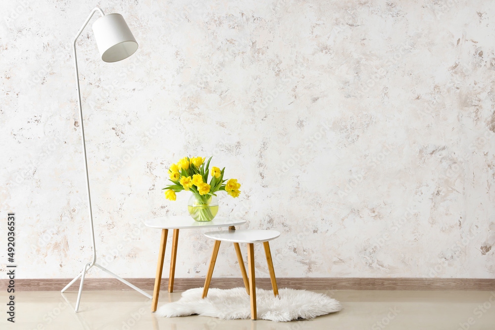 Coffee tables with flowers in vase and standard lamp near light wall