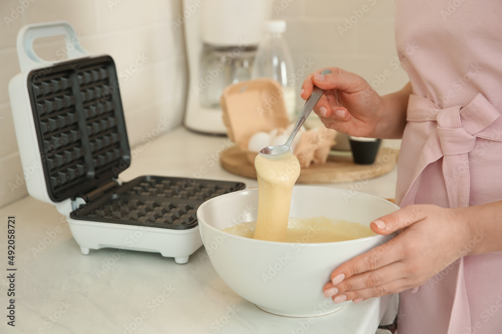 Woman preparing dough near Belgian waffle maker in kitchen, closeup