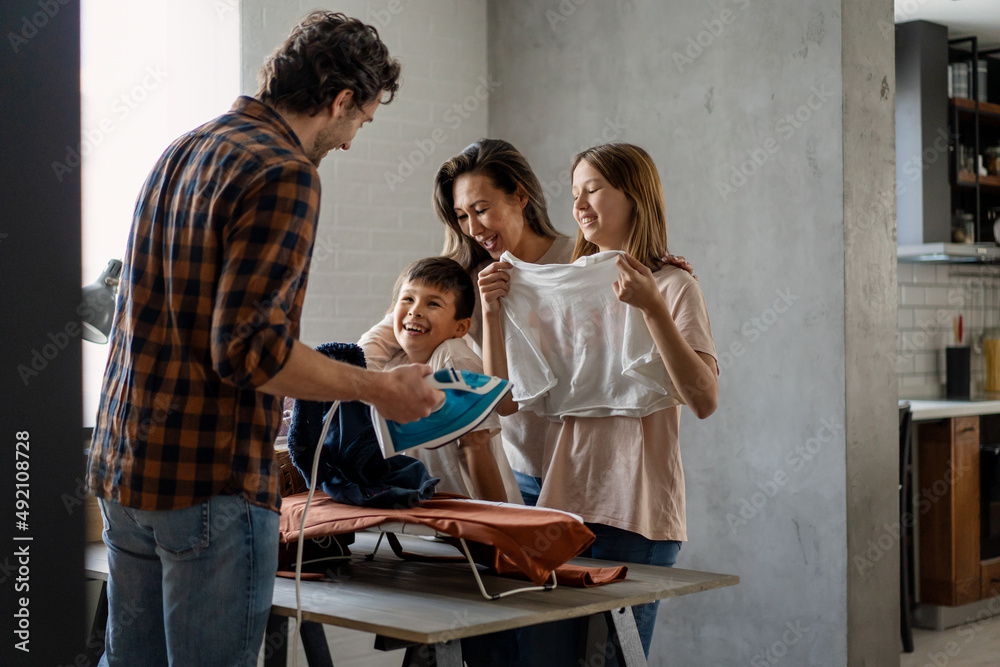 Happy mixed race family doing together domestic chores, ironing, household together at home.