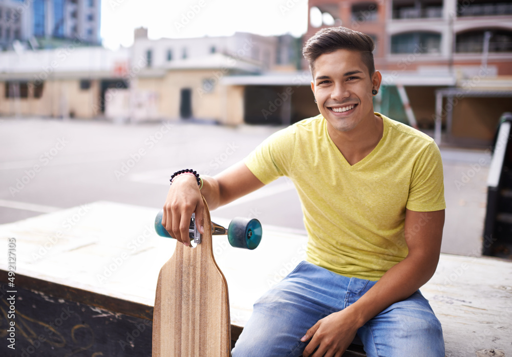 This is how I roll. Portrait of a young man sitting with his skateboard in the city.