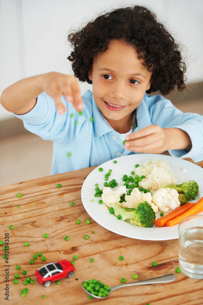 玩你的食物。一个可爱的小男孩把盘子里的豌豆扔得满桌子都是。