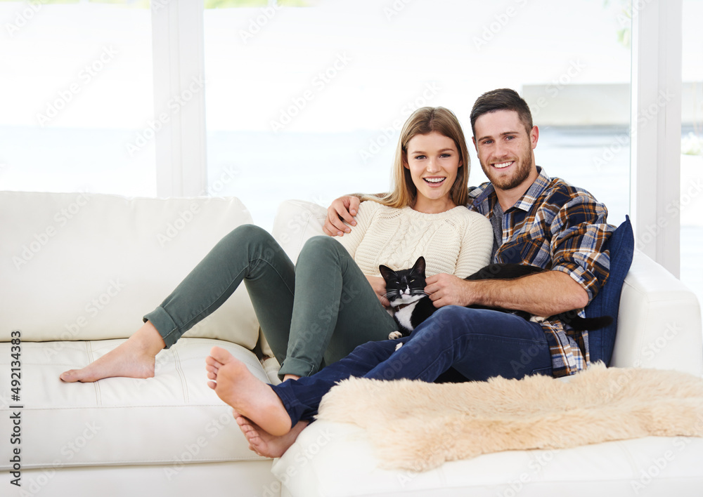 Hes a first fur baby. Portrait of a smiling young couple sitting with their cat on a sofa at home.