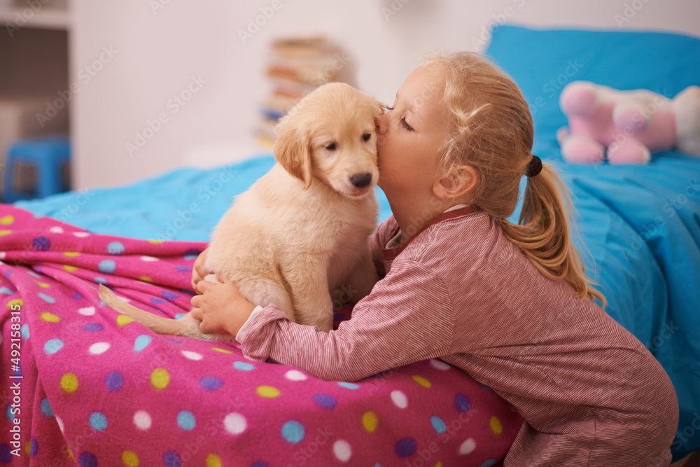 Kisses for her new friend. A cropped shot of a little girl kissing her puppy while it sits on her be