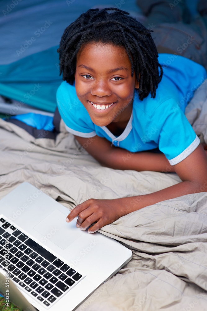 Kids are never far from the laptops. A young boy using his laptop while away on a camping trip.