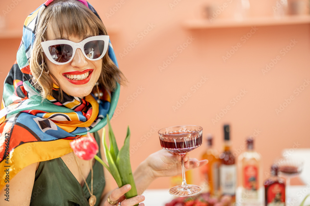 Portrait of a stylish caucasian woman in colorful shawl and sunglasses with flowers and drink celebr