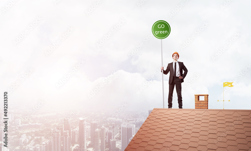 Businessman in suit on house top with ecology concept signboard. Mixed media