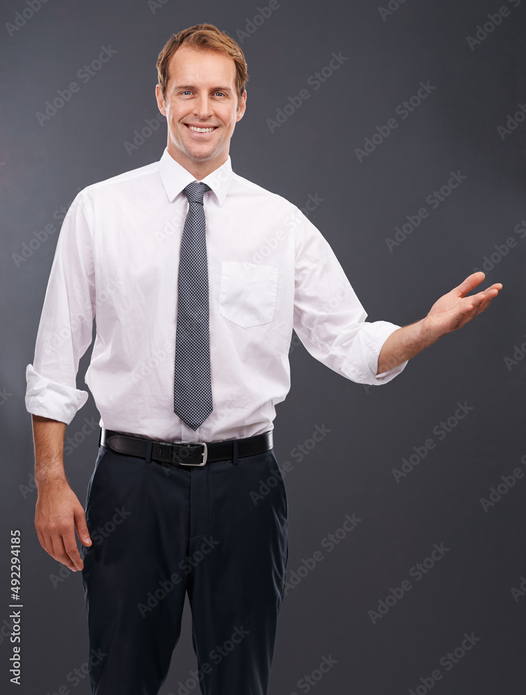 Let me show you what weve got. Portrait of a handsome young business man standing in front of a gray