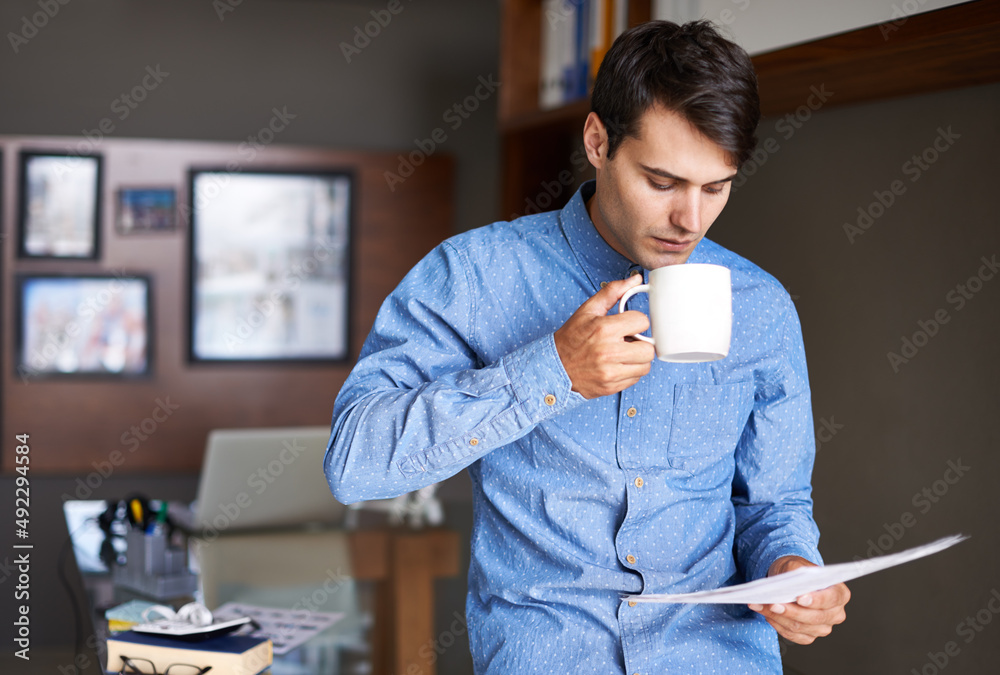 Coffee concentration. A young businessman drinking coffee while going through some paperwork.