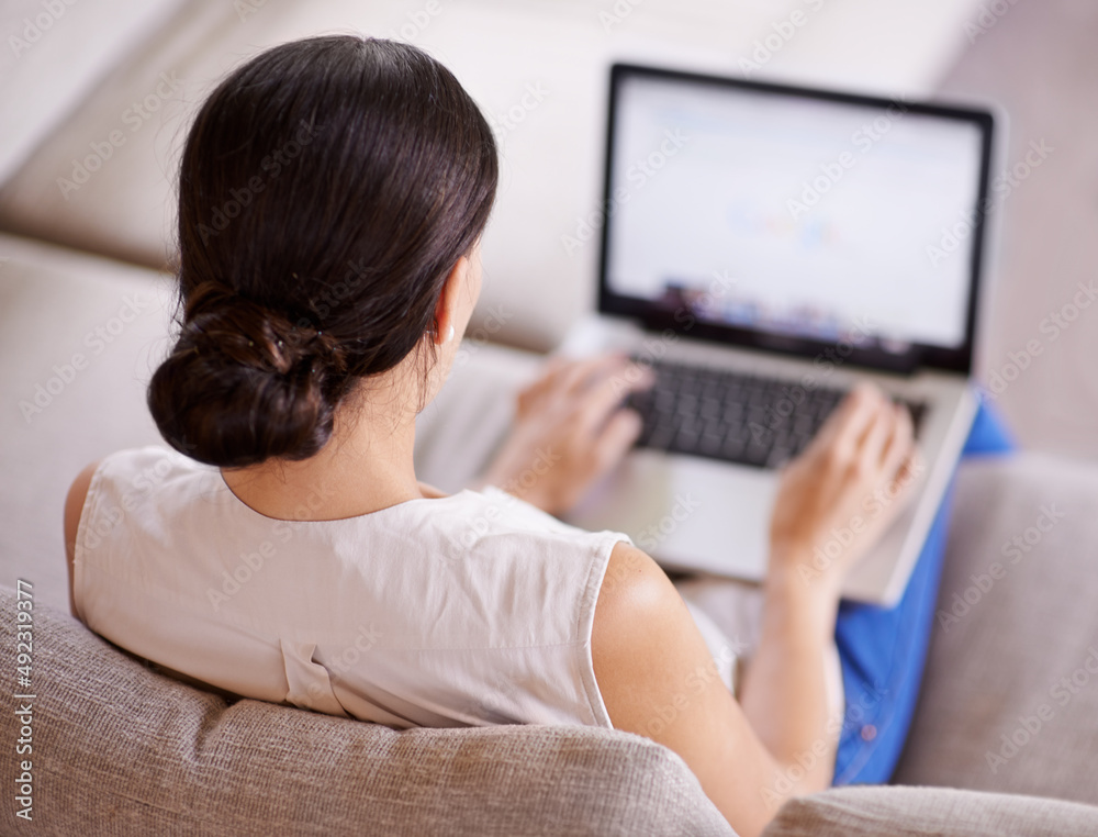 Taking in some surfing time. Over the shoulder shot of a young woman sitting on a sofa using a lapto