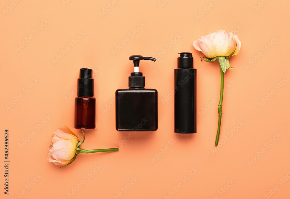 Bottles of cosmetic products and rose flowers on color background