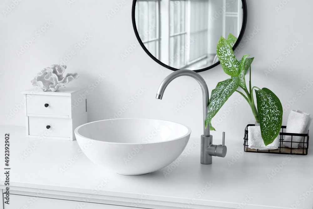 Modern sink with houseplant and drawers near light wall