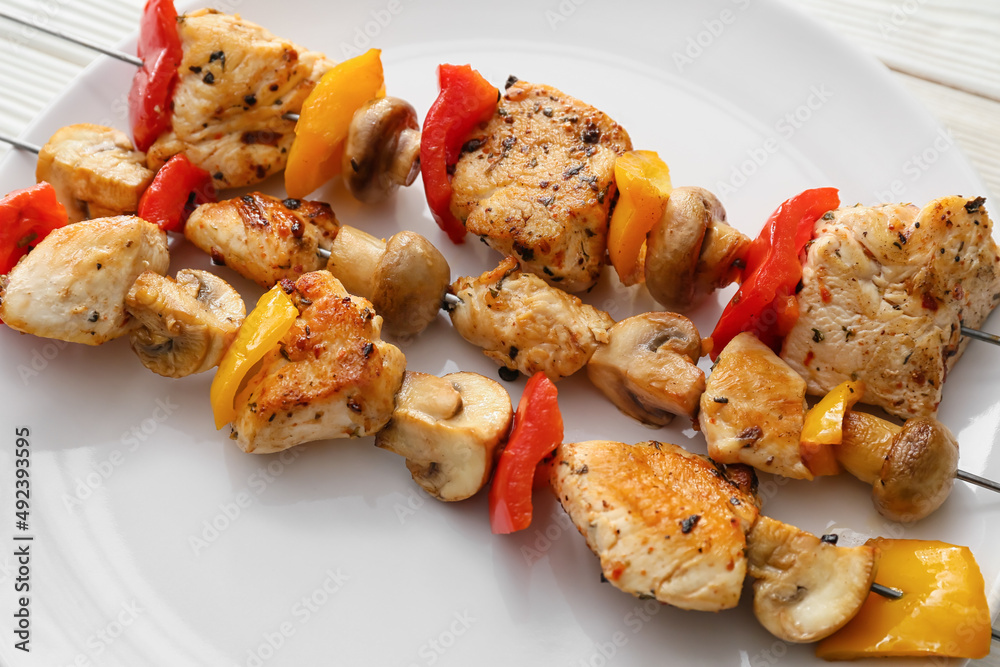 Plate of grilled chicken skewers with vegetables on table, closeup