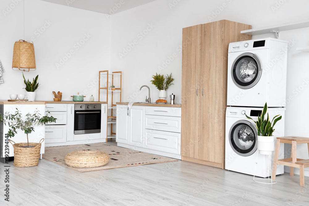 Interior of light kitchen with washing machines, white counters and cupboard