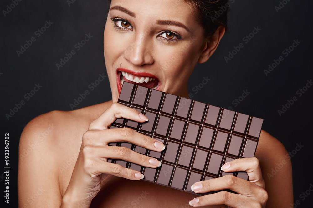 Yes, size matters. Studio shot of an attractive young woman biting into a slab of chocolate.