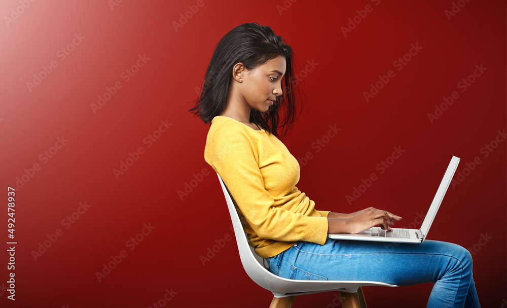 Deep in the world wide web. Studio shot of an attractive young woman using a laptop against a red ba