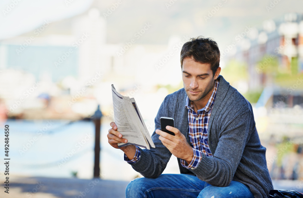 Reposting todays news. Shot of a handsome man holding the newspaper and using his phone outdoors.