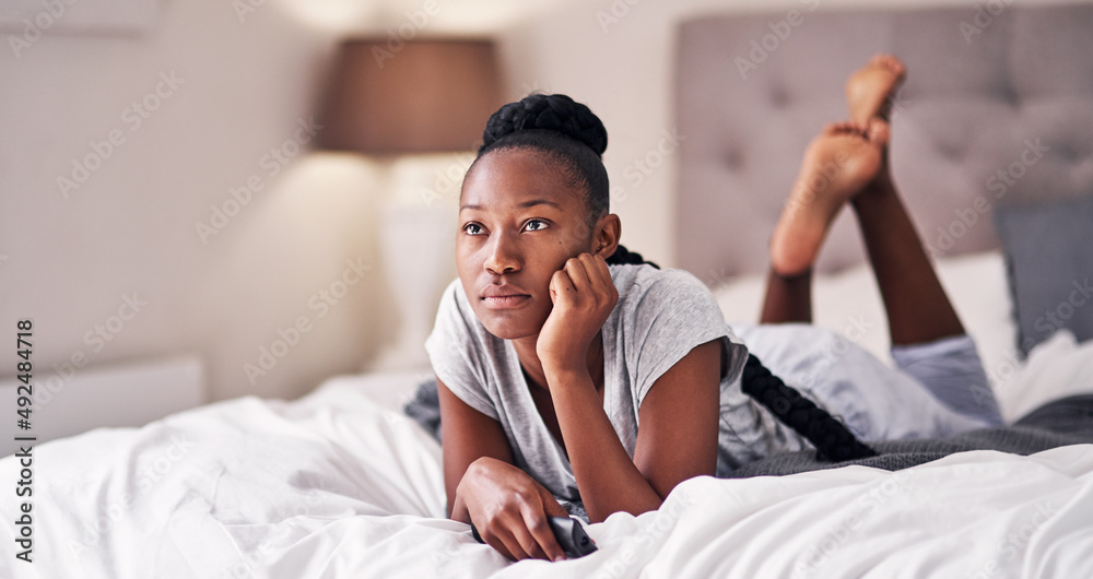 Im not doing anything but chill today. Shot of a young woman holding a remote control while lying on