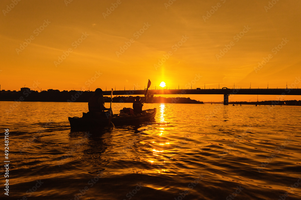 Silhouettes of people in kayak at sunset. Young married couple is boating on river.