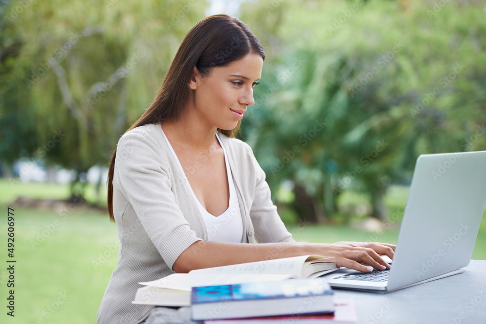 Working while enjoying nature. A young woman sitting in a park working on her laptop with a cup of c