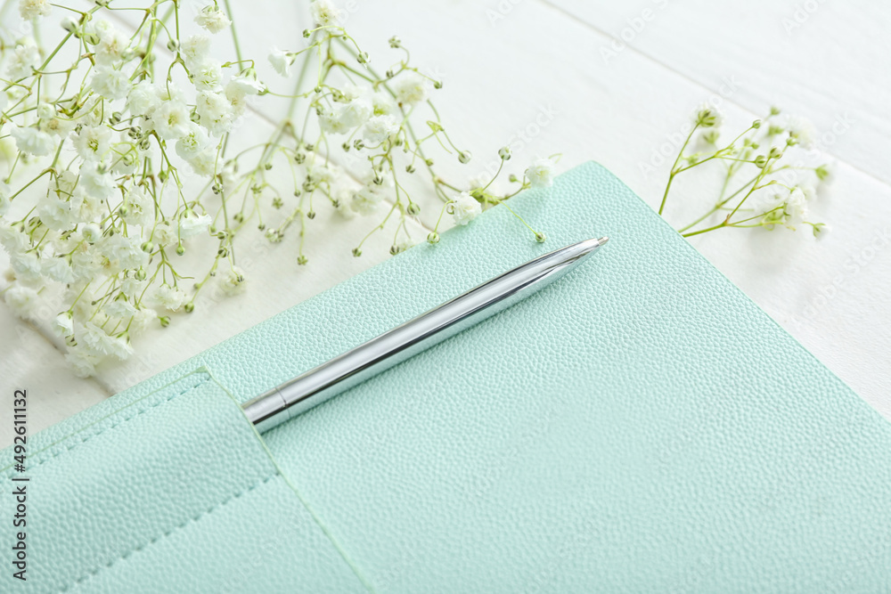 Stylish notebook with pen and gypsophila flowers on white wooden background, closeup