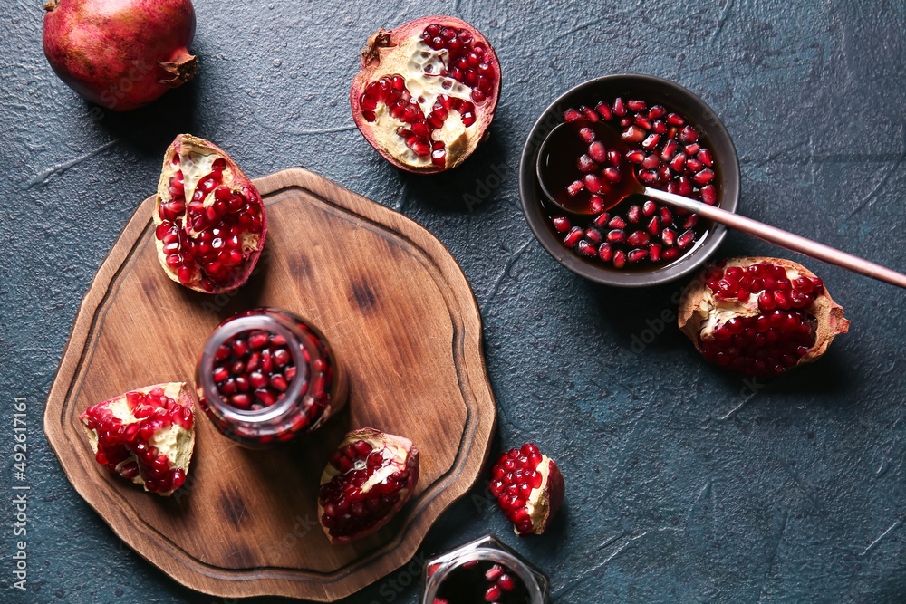 Jar and bowl of pomegranate molasses with fresh fruits on black background