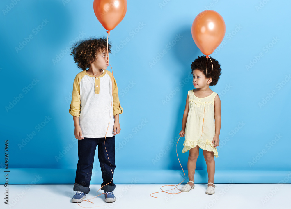 Look, no hands. Shot of a little girl and boy holding a balloon over a blue background.