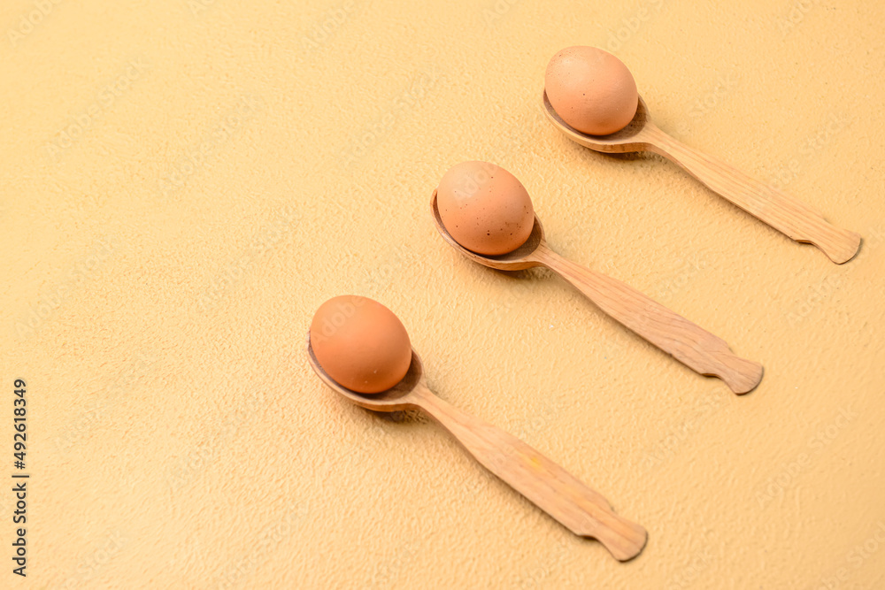 Spoons with fresh chicken eggs on beige background