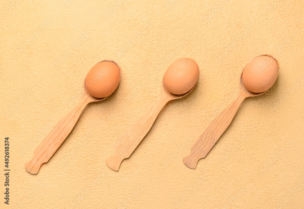 Spoons with fresh chicken eggs on beige background