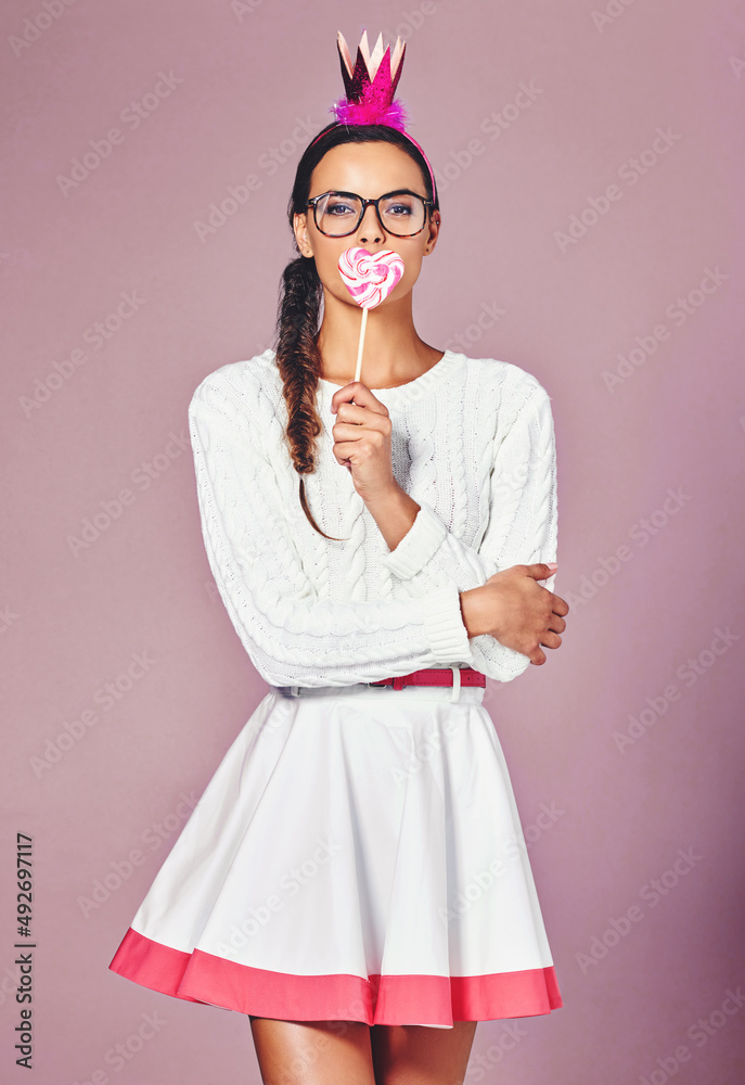 Dress how you want to be addressed. Shot of a young woman posing with a party crown and a lollipop a