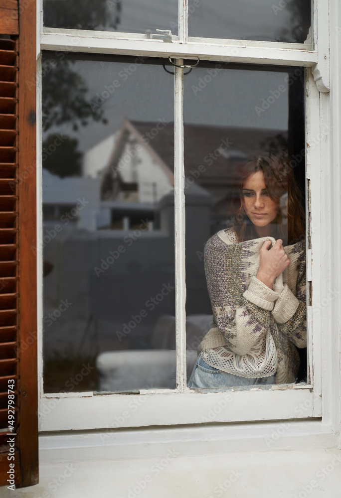 Small town yearning. Shot of a young woman looking out through a rustic farmhouse window.