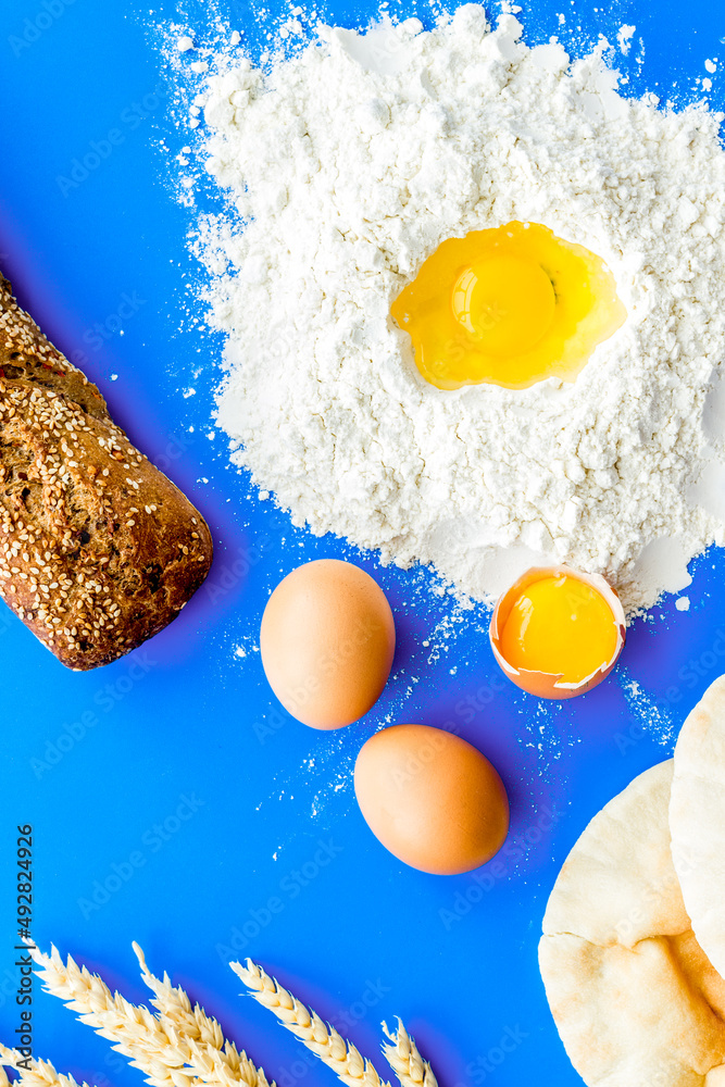 Baking background with eggs, flour and bread on blue table. Top view.