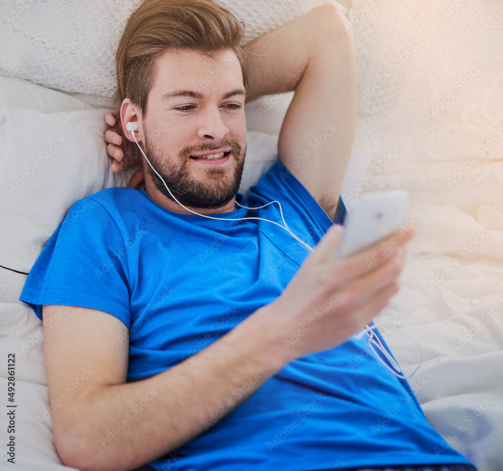 Downloading some new music. Cropped shot of a handsome young man listening to music while lying on h