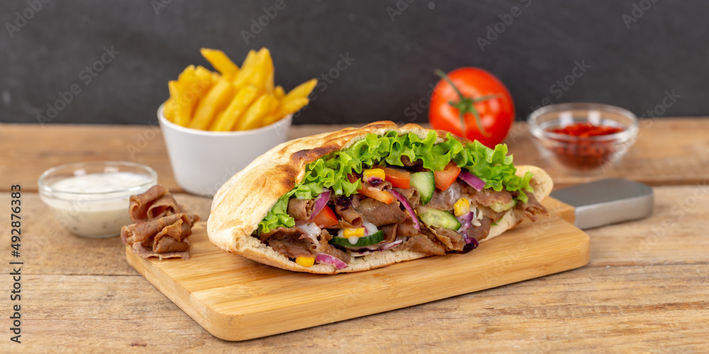 Döner Kebab Doner Kebap slice fast food in flatbread with French Fries on a wooden board panorama