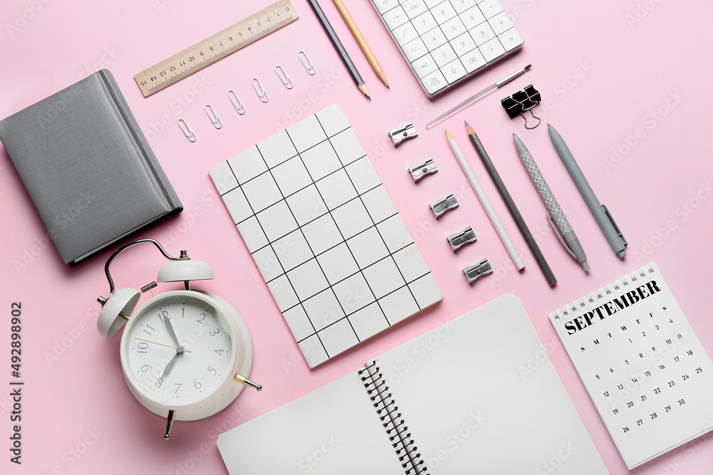 Composition with different stationery and alarm clock on pink background