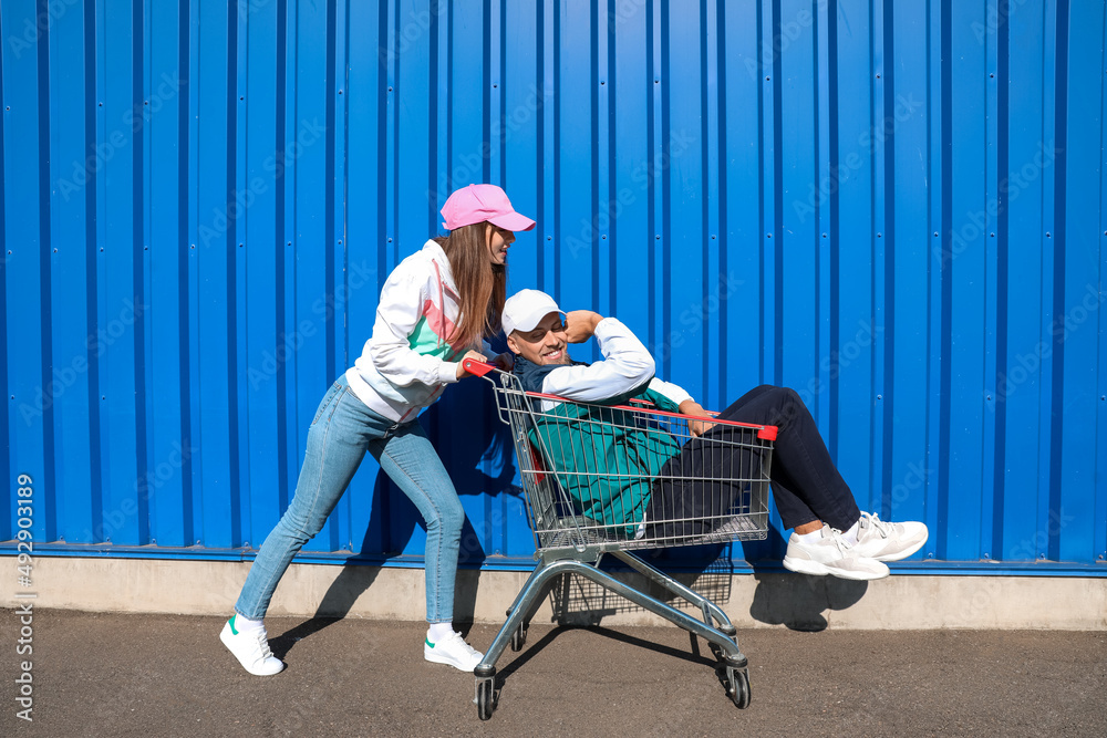 一名年轻女子在超市附近的购物车里骑着她的男朋友