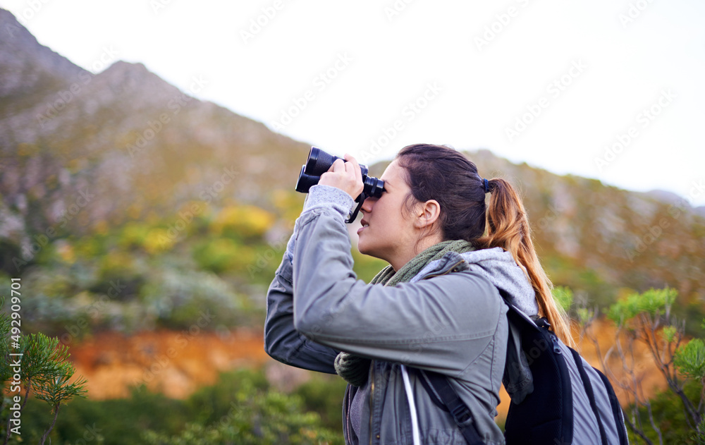 获得更好的视野。一位迷人的年轻女子在徒步旅行时通过双筒望远镜观看的照片。