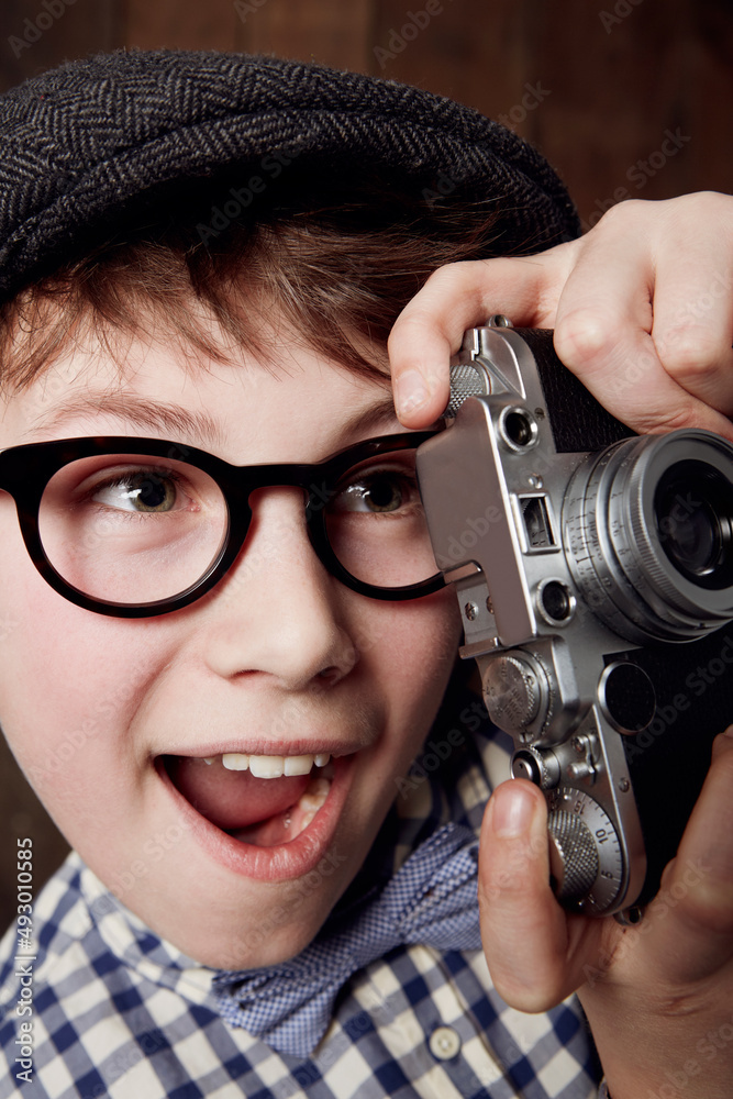 What a great shot. Young boy in retro clothing wearing spectacles and holding up his camera.