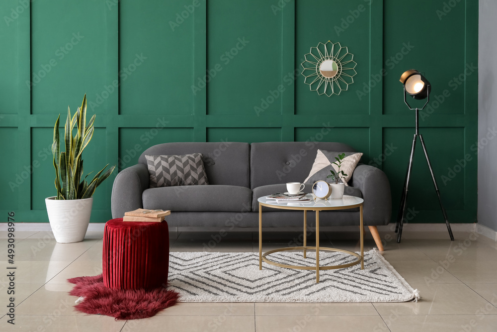 Interior of stylish living room with comfortable pouf, table and sofa near color wall