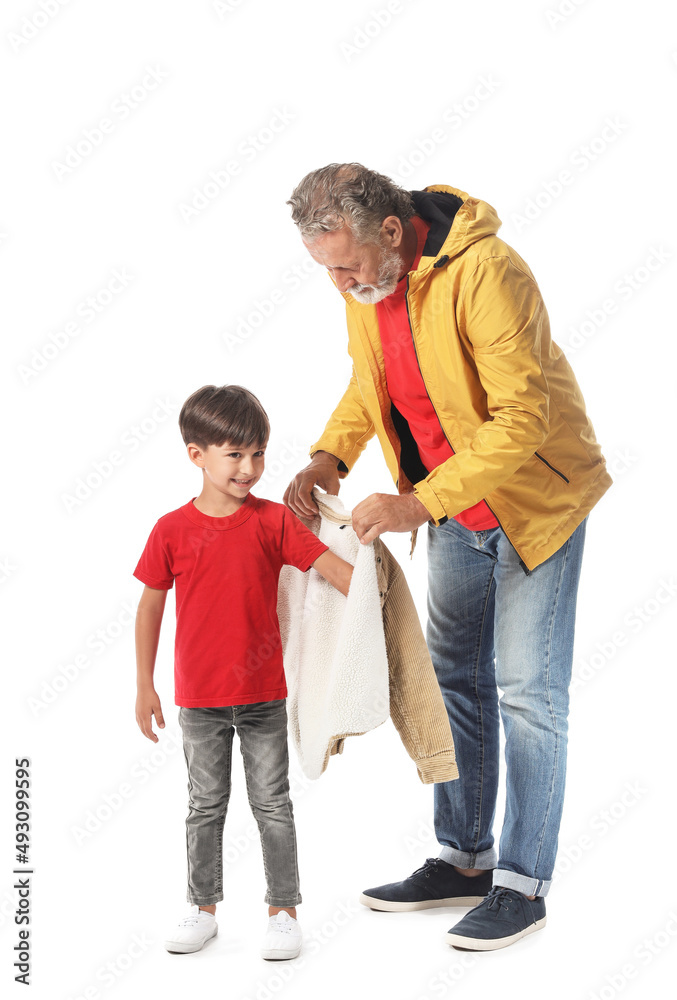 Senior man putting jacket onto his little grandson on white background