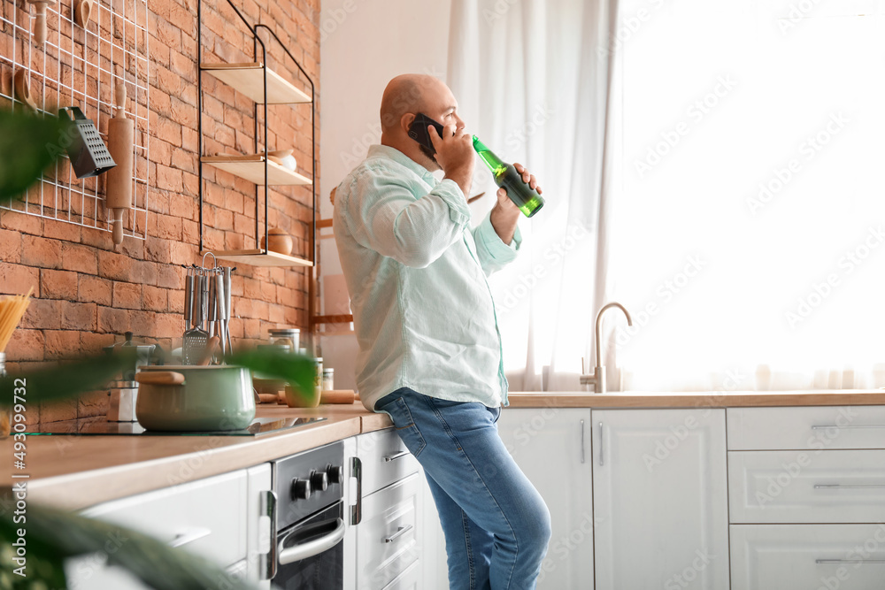 秃头男子在厨房喝啤酒打电话