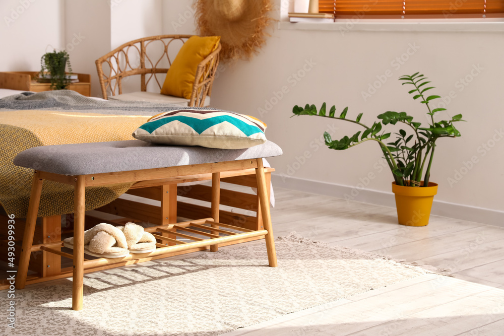 Modern bench with pillow and slippers in bedroom