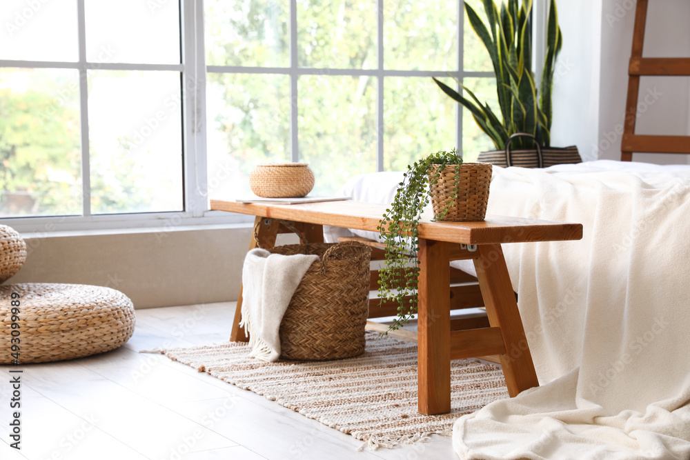 Wooden bench with basket and houseplant in interior of light bedroom